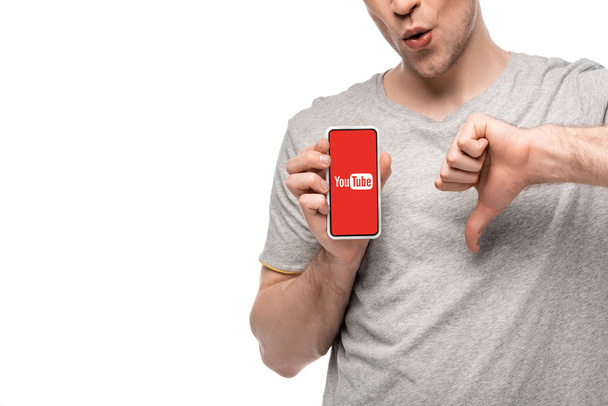KYIV, UKRAINE - MAY 16, 2019: cropped view of man showing thumb down and smartphone with youtube app, isolated on white - Photo, image
