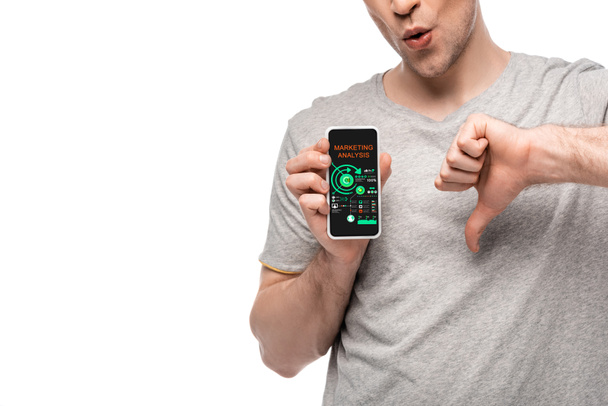 マーケティング分析アプリで親指を下に示す男とスマートフォンのトリミングされたビュー, 白に隔離 - 写真・画像