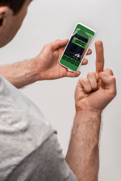vista recortada del hombre utilizando el teléfono inteligente con aplicación de reserva y mostrando el dedo medio, aislado en gris
 - Foto, Imagen