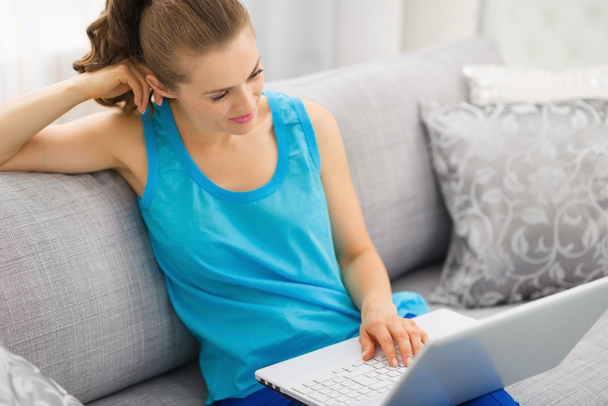Thoughtful young woman sitting on couch and using laptop - Φωτογραφία, εικόνα