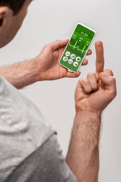 Ausgeschnittene Ansicht eines Mannes mit Smartphone mit Gesundheits-App und Mittelfinger, isoliert auf grau - Foto, Bild