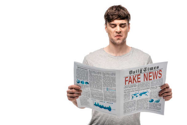 dissatisfied young man reading newspaper with fake news isolated on white - Фото, изображение