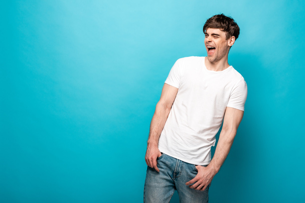 cheerful young man laughing while looking away on blue background - Foto, imagen