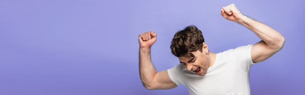 πανοραμική βολή του ευτυχισμένο νεαρό άνδρα που δείχνει νικητή χειρονομία απομονωθεί σε μπλε - Φωτογραφία, εικόνα