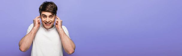 panoramic shot of cheerful man plugging ears with fingers isolated on blue - Photo, Image