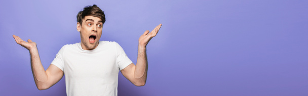 panoramic shot of handsome man showing shrug gesture on blue background - Photo, image