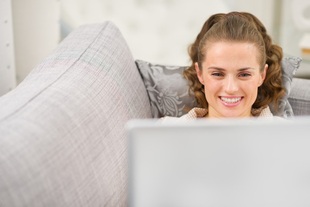 Happy young woman laying on divan with laptop - Photo, Image