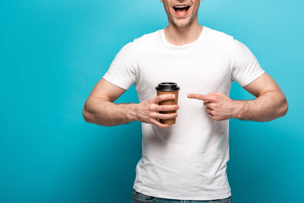 cropped view of smiling man pointing with finger at paper cup on blue background - Foto, Imagen