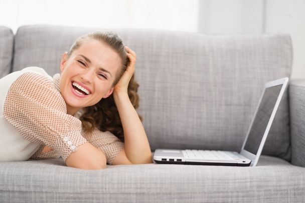 Giovane donna sorridente sdraiata sul divano con laptop
 - Foto, immagini