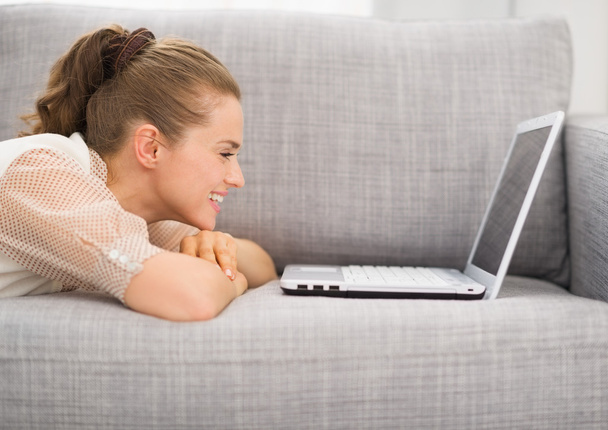 Happy young woman laying on sofa with laptop - Foto, afbeelding