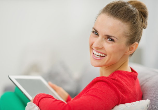 Smiling young woman sitting on couch and using tablet pc - Φωτογραφία, εικόνα