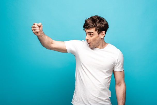 angry young man looking away and showing fist on blue background - Foto, immagini