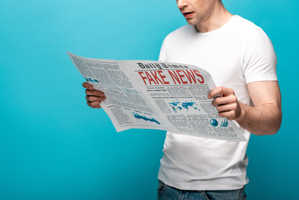 青い背景に偽のニュースで新聞を読んでいる男のトリミングされたビュー - 写真・画像
