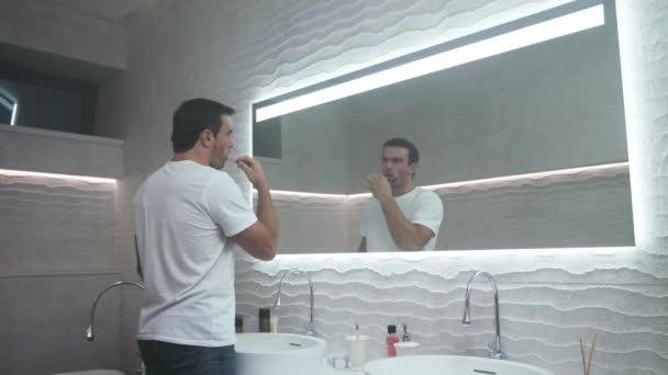 Gelukkige man poetsen tand in de badkamer. Geconcentreerde mannelijke persoon die tand draagt. - Video