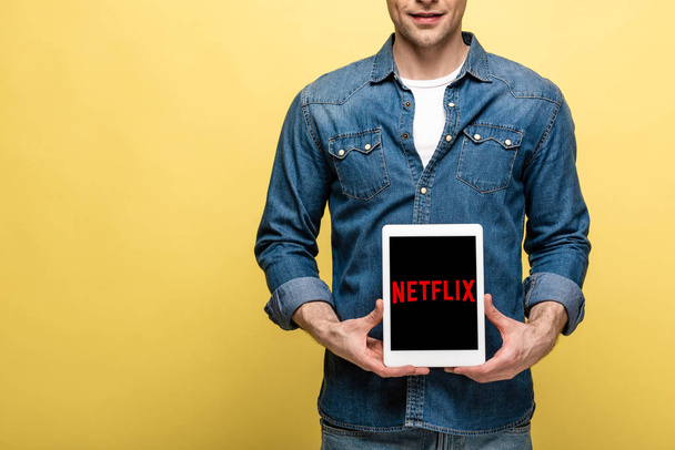 Kiev, Oekraïne-16 mei 2019: bijgesneden beeld van man in jeans kleren tonen digitale tablet met Netflix app, geïsoleerd op geel - Foto, afbeelding