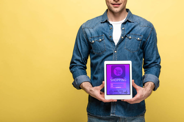 cropped view of man in denim clothes holding digital tablet with shopping app, isolated on yellow - Fotoğraf, Görsel