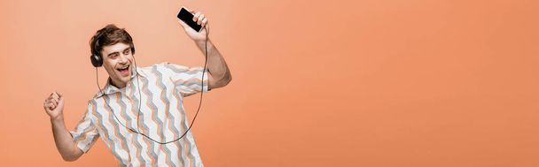 panoramic shot of happy young man dancing while listening music with headphones and smartphone on yellow background - Φωτογραφία, εικόνα