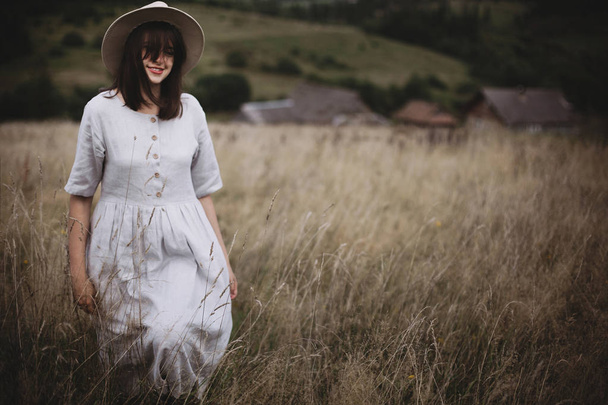 Elegante chica en vestido de lino y sombrero caminando entre hierbas y salvajes
 - Foto, imagen