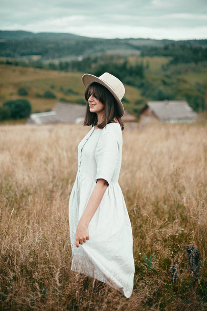 Κομψό κορίτσι σε λινό φόρεμα και καπέλο περπάτημα ανάμεσα σε βότανα και άγρια - Φωτογραφία, εικόνα