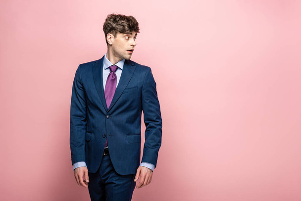 thoughtful businessman in suit looking away on pink background - Fotoğraf, Görsel