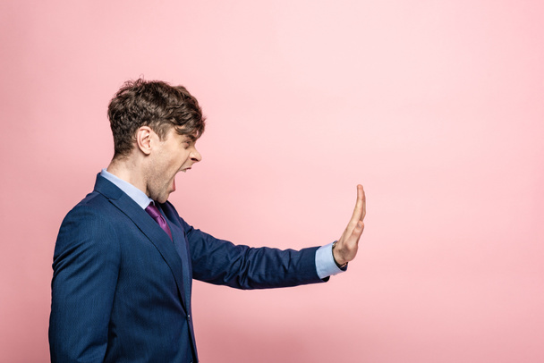 angry businessman quarreling and showing stop gesture on pink background - Foto, imagen