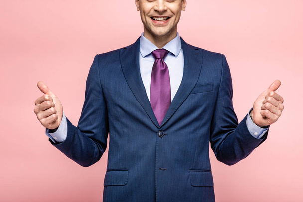 cropped view of smiling businessman showing thumbs up on pink background - Foto, immagini