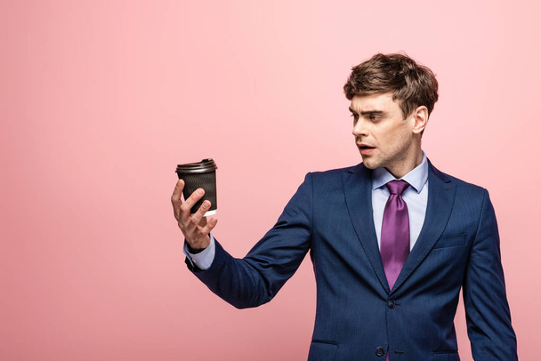 surprised businessman looking at disposable cup on pink background - Photo, Image