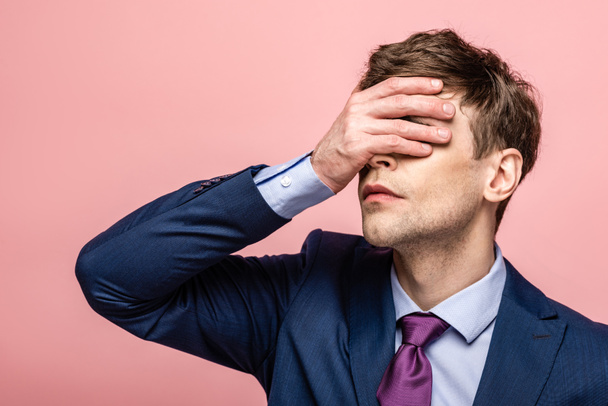 upset businessman covering eyes with hand isolated on pink - Foto, imagen