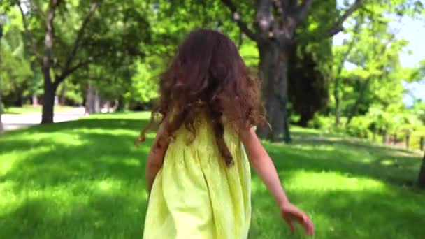 Happy little girl with yellow dress running barefoot on green grass in the park - Felvétel, videó