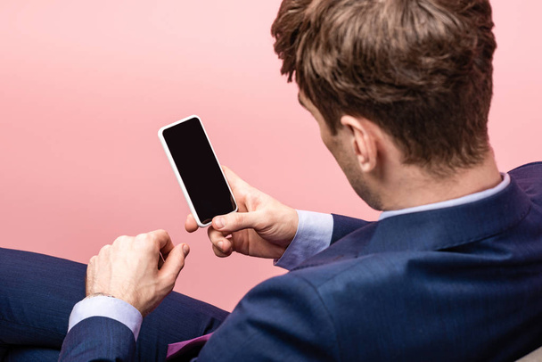 Achteraanzicht van zakenman zitten en houden smartphone met blanco scherm  - Foto, afbeelding