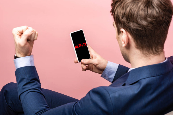 KYIV, UKRAINE - MAY 16, 2019: cropped view of successful businessman using smartphone with netflix app, isolated on pink - Fotoğraf, Görsel