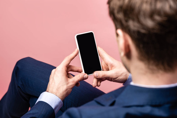 back view of businessman sitting and holding smartphone with blank screen isolated on pink - Fotografie, Obrázek