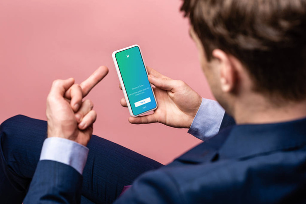 KYIV, UKRAINE - MAY 16, 2019: cropped view of businessman using smartphone with twitter app and showing middle finger, isolated on pink - Fotoğraf, Görsel