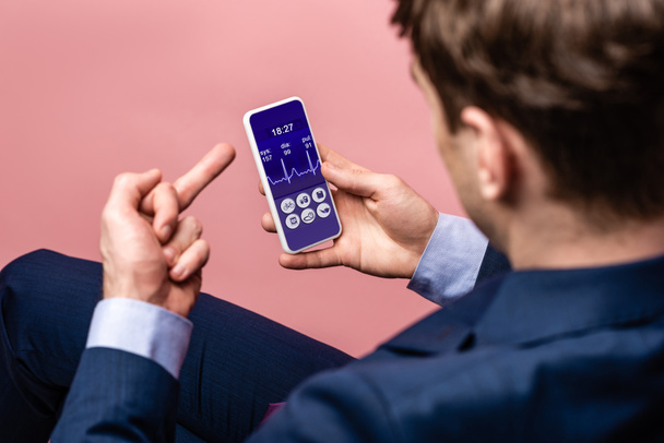 обрезанный вид бизнесмена с помощью смартфона с приложением здравоохранения, показывая средний палец, изолированный на розовый
 - Фото, изображение
