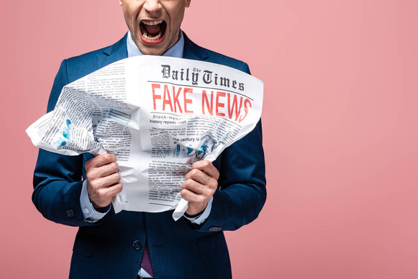разгневанный бизнесмен рушит газету с фейковыми новостями, изолированными на розовый
 - Фото, изображение