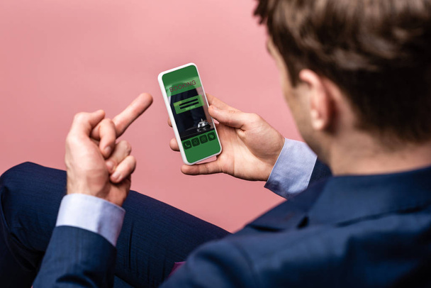 vista recortada de hombre de negocios utilizando el teléfono inteligente con aplicación de reserva, mientras que muestra el dedo medio, aislado en rosa
 - Foto, Imagen