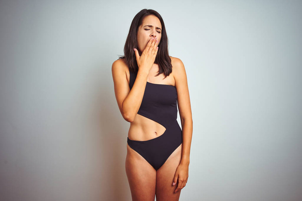 Beautiful woman wearing bikini swimwear over white isolated background bored yawning tired covering mouth with hand. Restless and sleepiness. - Zdjęcie, obraz