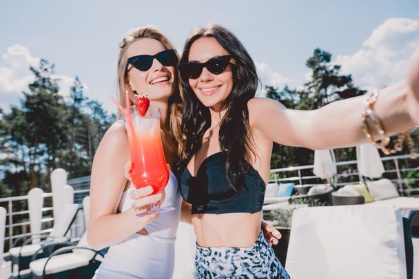 beautiful and happy brunette and blonde women with strawberry cocktail - Foto, afbeelding