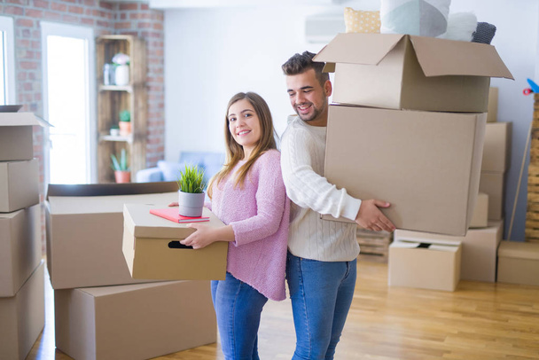 Young beautiful couple in love moving to new home, holding cardboard boxes very happy and cheerful for new apartment - Photo, Image