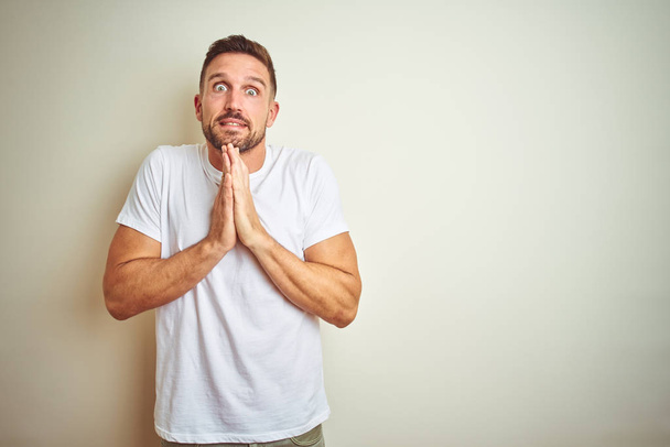 Young handsome man wearing casual white t-shirt over isolated background praying with hands together asking for forgiveness smiling confident. - Фото, изображение