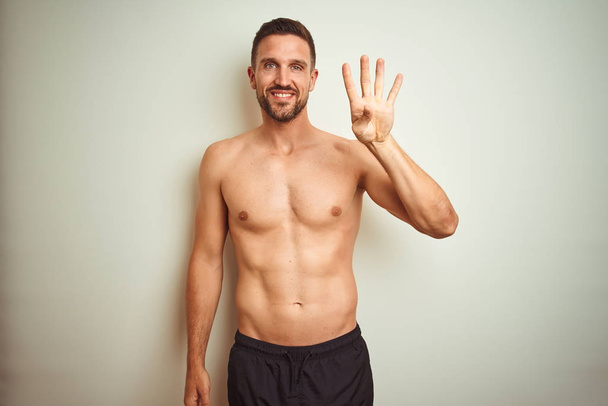 Homem sem camisa bonito jovem sobre fundo isolado mostrando e apontando para cima com os dedos número quatro, sorrindo confiante e feliz
. - Foto, Imagem