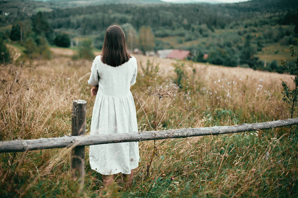 Chica con estilo en vestido de lino de pie en la cerca de madera envejecida entre
  - Foto, imagen