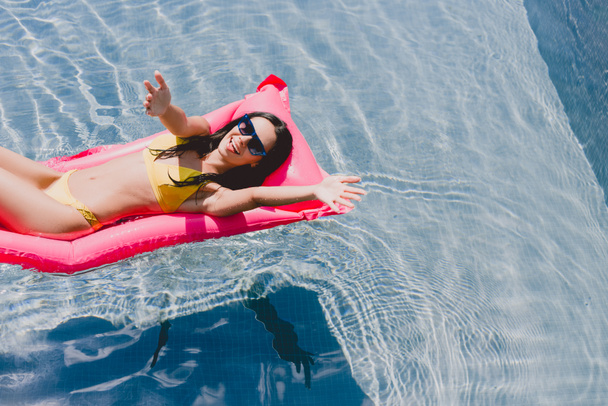gelukkige brunette vrouw met uitgestrekte handen op zwembad float in zwembad - Foto, afbeelding