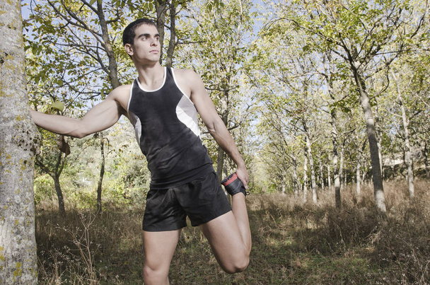 Joven corredor hombre calentando piernas en el bosque
 - Foto, Imagen