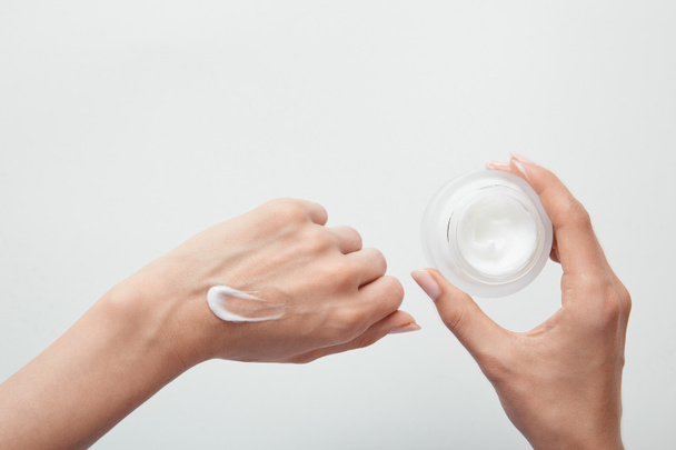 cropped view of woman applying cream on skin and holding jar isolated on white - Φωτογραφία, εικόνα