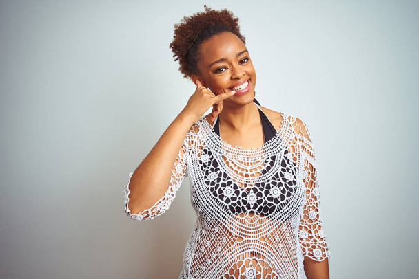 Jonge Afro-Amerikaanse vrouw met afrohaar die een bikini draagt over een witte, geïsoleerde achtergrond, glimlachend, telefoongebaar makend met hand en vingers, zoals telefoneren. Communicatie concepten. - Foto, afbeelding