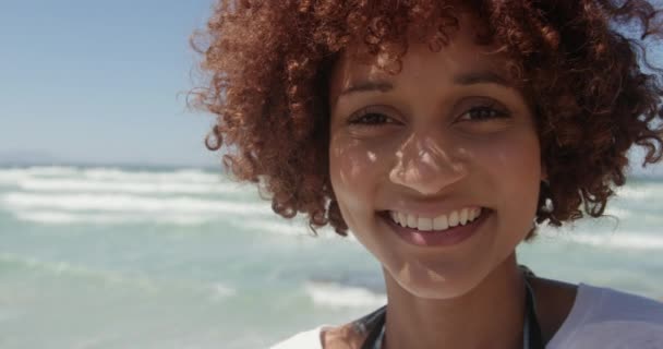 ビーチでカメラを見ているアフリカ系アメリカ人女性の正面図。彼女は微笑んでカメラ4kを見ている - 映像、動画