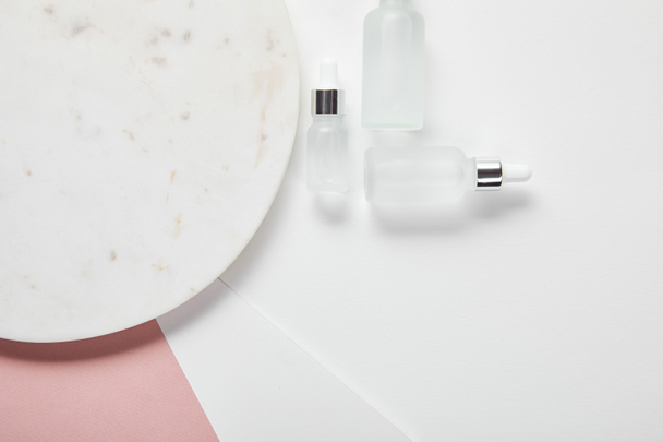 vista superior de garrafas de vidro cosmético perto da placa na superfície rosa branca
 - Foto, Imagem