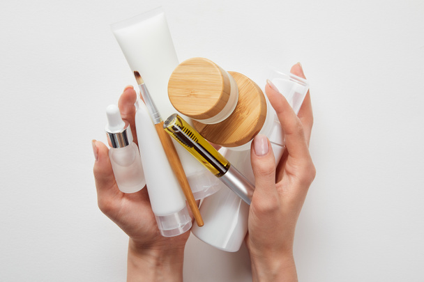 ostříhané zobrazení ženských rukou s kosmetickými prostředky v trubkách, rozprašovačích, lahvích a nádobě izolované na bílém - Fotografie, Obrázek