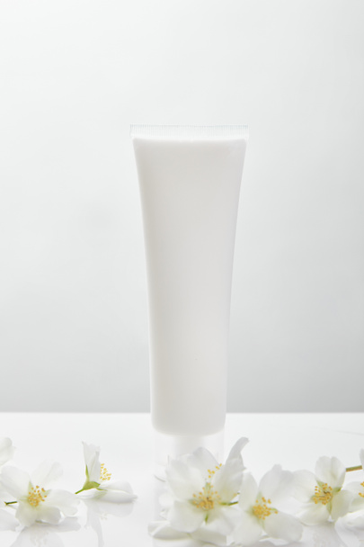 jasmine flowers on white surface near cosmetic cream in tube - Photo, Image